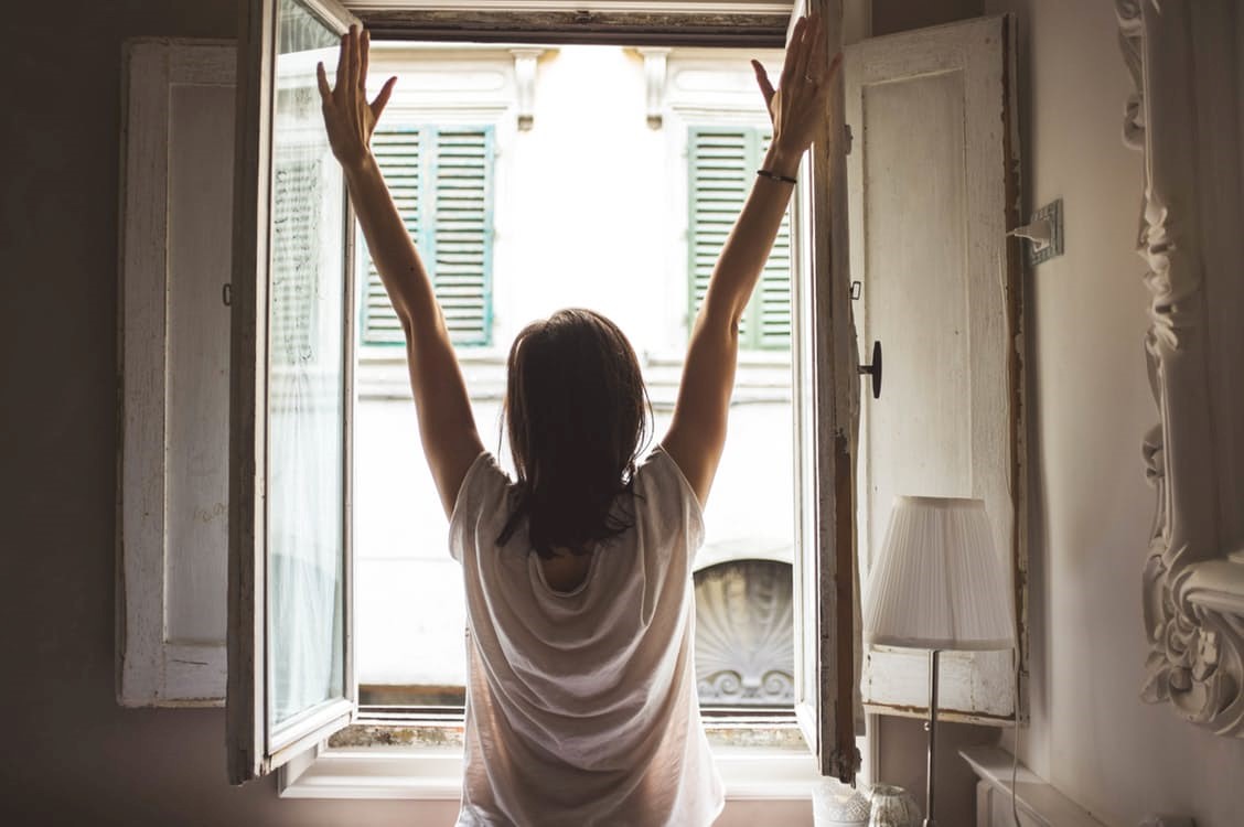 Eine Frau wacht auf, streckt ihre Arme und blickt dabei aus dem Fenster