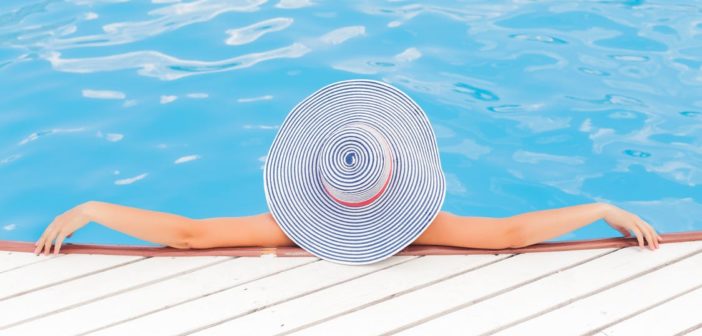 A bird’s eye view of a women in a large sun hat lounging in the shallow end of a pool