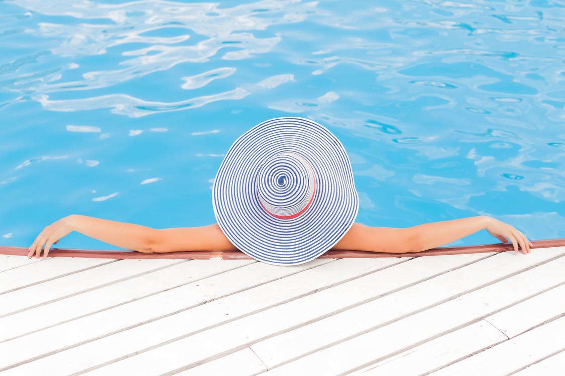 Θέα μιας γυναίκας που φοράει ένα μεγάλη καπέλο για τον ήλιο και χαλαρώνει στα ρηχά μιας πισίνας